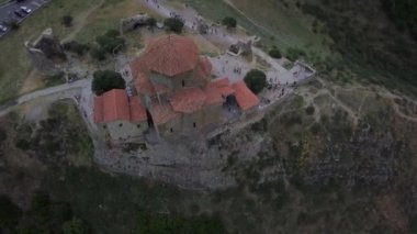 Tiflis, Gürcistan - 14 Haziran 2018: Önünde araba ve otobüslerin bulunduğu bir otoparkın bulunduğu tepede kırmızı bir kiremit çatısı bulunan Jvari Stone Manastırı. İnsanlar tapınağın etrafında dolaşıyor..