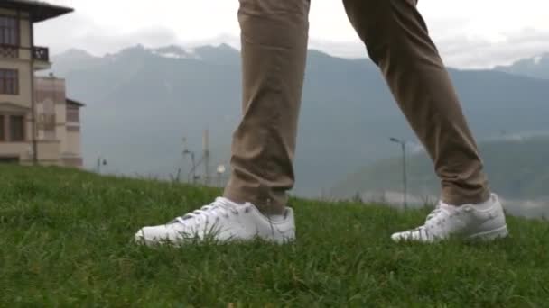 Man Vita Sneakers Och Ljusbrun Byxor Klättrar Grönt Gräs Och — Stockvideo