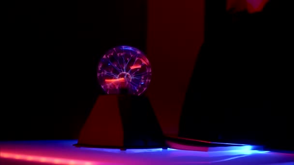 白いテーブルの上の暗い部屋で 青い光で照らされ 稲妻のボールです 近くに立っている人々は 彼の隣のテーブルの上に手のひらを置いた パノラマ撮影 パズルの概念 — ストック動画