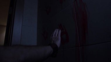 Adam elini odadaki beyaz bir duvara kazınmış kırmızı bir avucuna koyar ve sonra çıkarır. Duvarda bir sürü el izi ve lekeli boya var. Bulmaca kavramı.