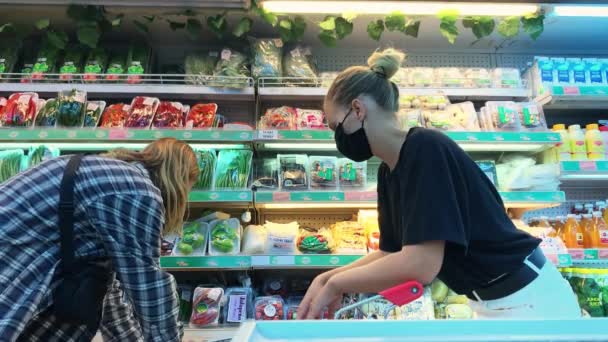 一家商店里的一个金发白人女孩站在一个架子旁边 她的架子上放着香草和蔬菜 金发男人走过去 拿着胡萝卜递给她 把它放在推车里 然后他们就离开了 Covida 19期间的购物 — 图库视频影像