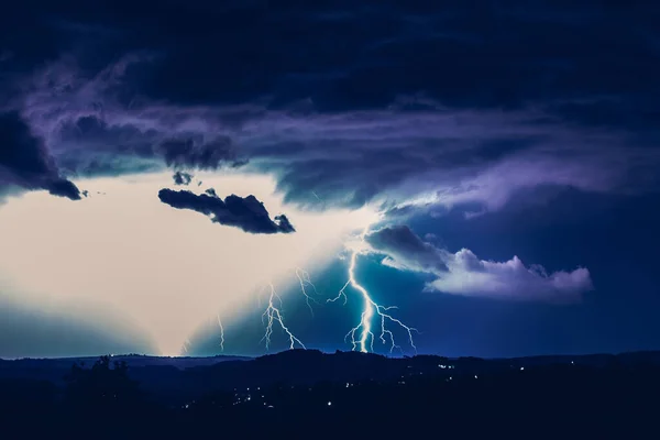 Night landscape on a background of thunderstorms. Rural silhouette and clouds with lightning flashes