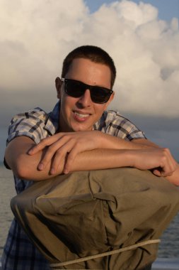 Genç adam tarafından katranlı muşamba kaplı gyro Tekrarlayıcı yakınındaki poz. Resim arka plan günbatımı, güzel bulutlarda, çekilen. Turist broşürü için kavram, yayınları ile deniz konular olarak kullanılan.