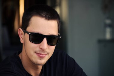 Siyah gömlek giymiş bir kapı üzerinde oturan bir genç adam. Gözlük tekerlekli ev yan kanat yansımasıdır. Bulanık arka plan bir kargo gemisi tekerlek evi iç kısmıdır.