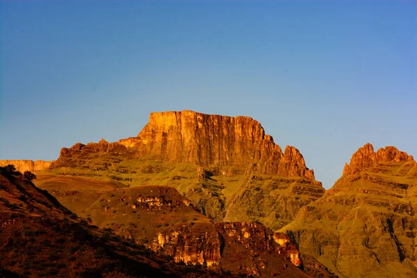 僧侶のカウル ドラケンスバーグ山脈 南アフリカ共和国 黄金の光の中青空の晴れた日の早朝撮影と呼ばれる山の風光明媚な屋外景観画像を色します — ストック写真