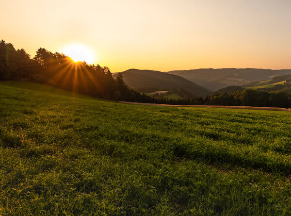 Warm colored bright golden epic sunrise rural panoramic landscape image with a wide view over fields,forest,hills and valleys towards the horizon