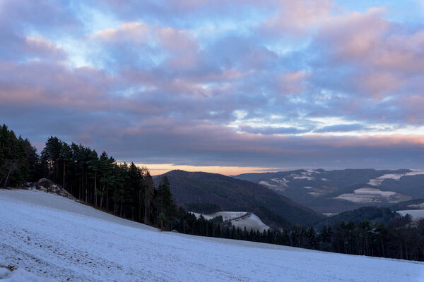 Живописный панорамный цвет сельской зимней сельской местности в австрийском холмистом ландшафте с лесом, полями и снегом и видом на горизонт, голубое небо с облаками
