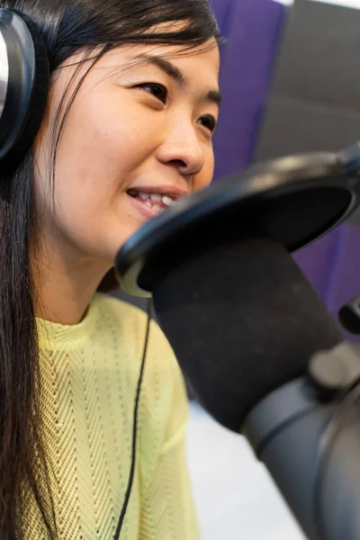 cheerful asian woman radio DJ with headphones in the broadcasting studio. Close up picture.