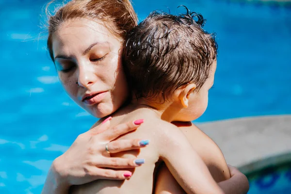 Detail of a woman\'s face with a calm expression as she hugs a child inside a pool with the nails painted and a ring