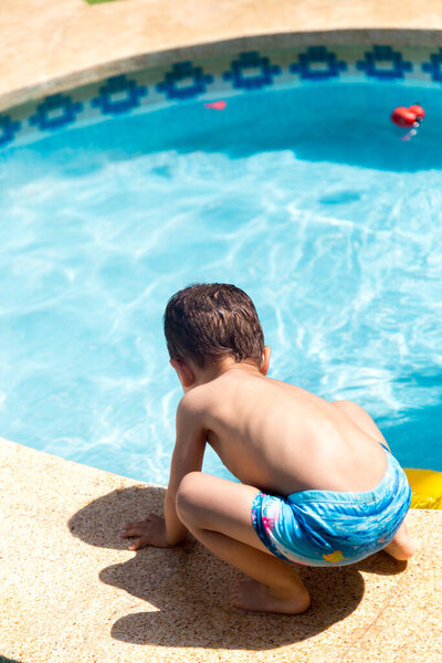 Кавказский мальчик спиной вниз играет в воде на краю бассейна в солнечный день
