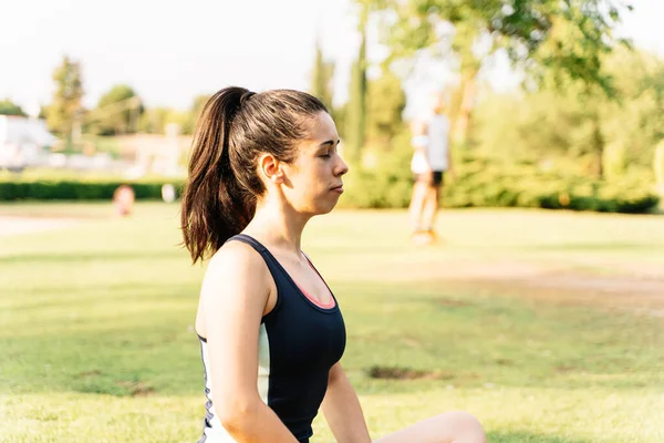 Profile of a woman in sportswear meditating in a park with her eyes closed on a sunny day