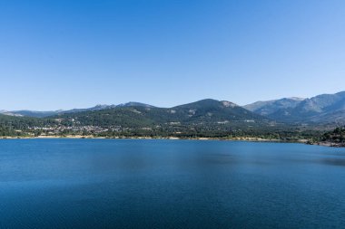 Madrid 'in Sierra dağlarındaki Navacerrada' da yeşil dağlarla çevrili bir gölün panoramik manzarası.