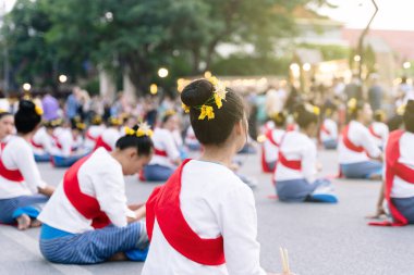 Chiang Mai, Tayland, 10 Kasım 2019: Geleneksel Tayland elbiseli, kırmızı bantlı ve kafasında çiçekler olan bir grup genç kadın sokakta yerde oturuyorlar.