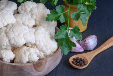 Sarımsak ve biber, tahta kaşık ile taş arduvaz arka plan üzerinde ahşap kase kesilmiş beyaz karnabahar Üstten Görünüm.