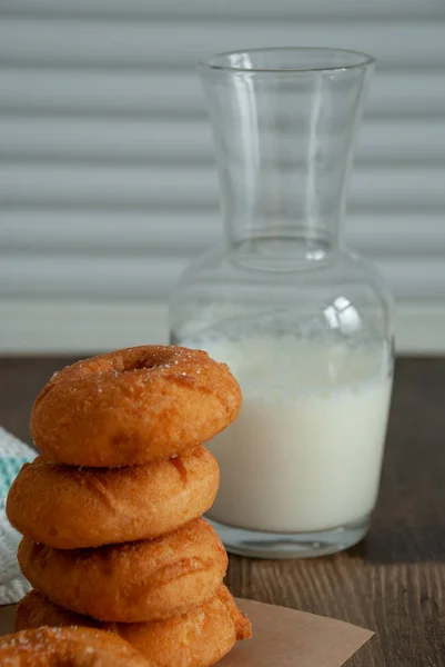 Close-up of donuts in stack with bottle of milk on wooden background and white wall