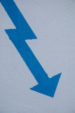 Duvara boyanmış beyaz arka plan üzerinde dikey olarak eğilmiş mavi ok