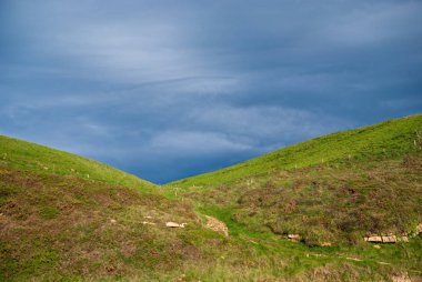 Cantabria, İspanya, Avrupa kıyılarında fırtınalı mavi gökyüzü ile gün batımında yeşil çayırmanzara