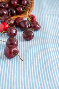 Kopya alanı ile dikey beyaz çizgili mavi masa örtüsü arka plan üzerinde sepet kiraz üst görünümü