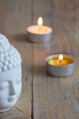 Dikey olarak yıpranmış ahşap masa üzerinde beyaz buda figürü ve mumların yakın çekim