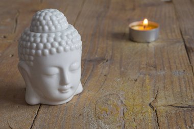 Yatay olarak yıpranmış ahşap tahta üzerinde beyaz buda figürü ve mum yakın çekim