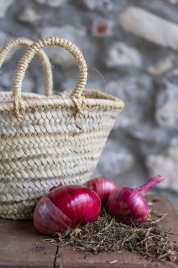 Ahşap masa ve dikey taş arka plan üzerinde sepet ile çim üzerinde sebze bahçesinden mor soğan üst görünümü