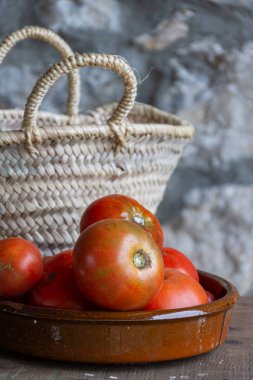 Ahşap masa, sepet ve dikey odaklanmamış taş arka plan üzerinde kil kase meyve bahçesi domates üst görünümü