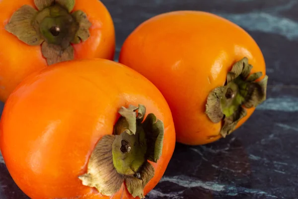 Yatay olarak koyu mermer üzerinde üç turuncu kakinin yakın çekimi