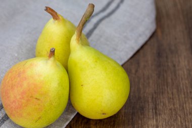 Gri bulaşık bezi üzerindeki küçük yeşil armutlar ve odaklanmamış arka plan tahtasının üst görüntüsü