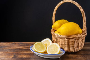 Tahta masa ve siyah arka planda yarım limon bulunan sepetteki limonları dikey olarak kopyala.