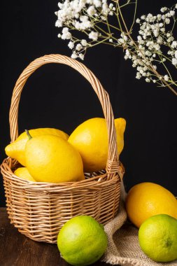 Limonlu sepetin üst görüntüsü, limonlu çuval bezi, ahşap masa, odak dışı beyaz çiçekler, siyah arka plan, dikey