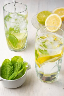 İki bardak buzlu su, limon ve limon dilimlerinin üst görüntüsü, yarım limon ve naneli, dikey.