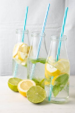 Mavi kamış, su, limon ve nane dilimli üç şişenin köşegen üst görüntüsü, yarım limon, beyaz arka plan, dikey