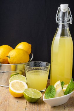 Limonata, cam, limon, nane ve tüm limonları metal kovada, ahşap masa ve siyah arka planda, dikey