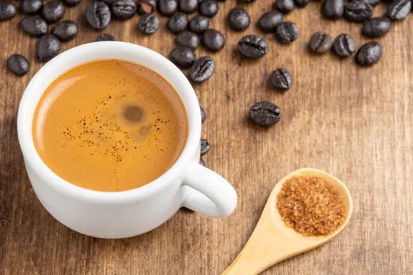 コーヒー豆と茶色の砂糖 水平と木製のスプーンで木製のテーブルの上にコーヒーと白カップのトップビュー — ストック写真