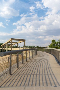 Arka planda beton köprü olan çitlerin gölgeli yolu, beyaz bulutlu mavi gökyüzü, günbatımında, dikey