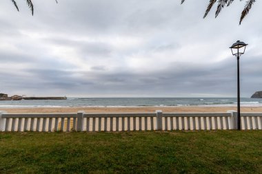 Beyaz çit ve sokak lambası manzarası. Arka planda deniz ve kumsal var. Comillas, Cantabria, İspanya 'da bulutlu bir öğleden sonra.