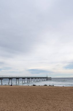 Deniz ve sahil üzerindeki yaya köprüsünün açısal görüntüsü, bulutlu bir günde, Badalona, Katalonya, İspanya, dikey