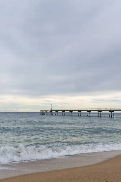 Landscape of beach with walkway over the Mediterranean Sea, a cloudy day, in Badalona, Catalonia, Spain, in vertical
