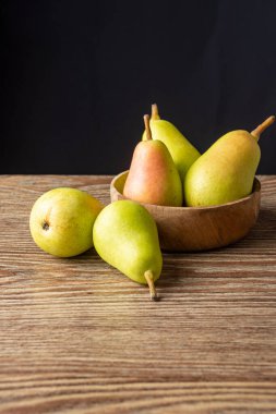 Ahşap kasedeki birkaç ercolina armutunun üst görüntüsü, tahta masa üzerinde ve dikey olarak siyah arkaplan, kopyalama alanı ile