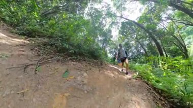 Ağaçların arasından süzülen güneş ışığıyla dolu yemyeşil bir orman yolunda yürüyen bir kadın, toprak yola bakıyor, geniş bir açı, orman keşfi kavramı.