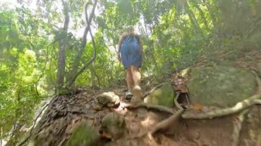 Orman yolunda yokuş yukarı yürüyen mavi kot elbise ve şapkalı bir kadın, tırmanırken aşağıdan vurulmuş, Orman Macerası Konsepti.