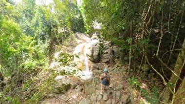 Ormanın sonunda kayalar ve ormanlarla çevrili bir şelaleye ulaşan kadın dereye bakıyor, geniş açılı, Doğa İstikameti kavramı.