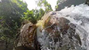 Düşük açılı güçlü şelale manzarası ormanda kayalık uçurumun kenarında kadının ayakları derenin üstünde, dinamik hareket, taze su enerjisi konsepti