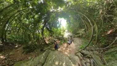 Kadın ve erkek yukarıdaki kavisli ağaçlarla kayalık orman patikalarından inerken, kadın onları uzaktan takip ediyor, enlemli küresel manzara, Doğal Trek Konsepti