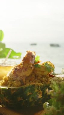 Dikey video. Ananasın içinde taze marul ve buzlu içecekle servis edilen karides kızartması. Plajın yakınındaki ahşap tepside. Yaklaş Tropikal Deniz Ürünleri Tabağı Konsepti.