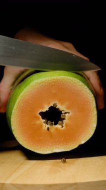 Dikey video. Ellerin Yakın Çekimi Olgun Papaya 'yı İkiye Dilimliyor Tohumları Gösteriyor ve Tahta Kesme Tahtasındaki Canlı Turuncu Et Sağlıklı Yeme Konsepti