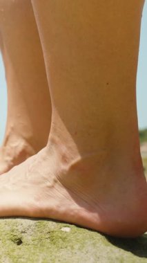 Dikey video. Yuvarlak Kayalıklarda Çıplak Ayaklı Kişi Yakından Bakış ve Sığ Deniz Altında Parlak Gökyüzü Yandan Alçak Açı, Plaj Konseptinde Özgürlük