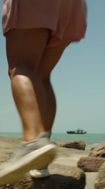 Dikey video. Sneakers 'lı Kadın Deniz kenarında Büyük Kayalıklarda Yürüyor Düşük Açılı Hareket Bulanıklığı, Macera Konsepti