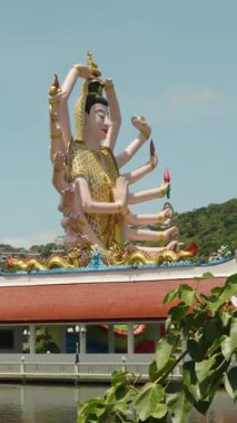 Dikey video. Geniş Açı Su ve Ağaçlarla çevrili Büyük Çoklu Silahlı Tanrıça Heykeli, Wat Plai Laem Samui Manevi Dönüm Noktası