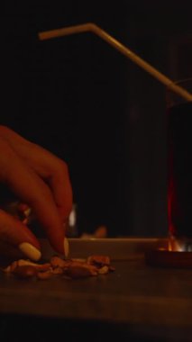 Parmaklar, TV 'nin düşük açılı gevşek zaman kavramını izlerken Masada İki bardak koyu içecek ve mum ışığıyla karışık fındık topluyor